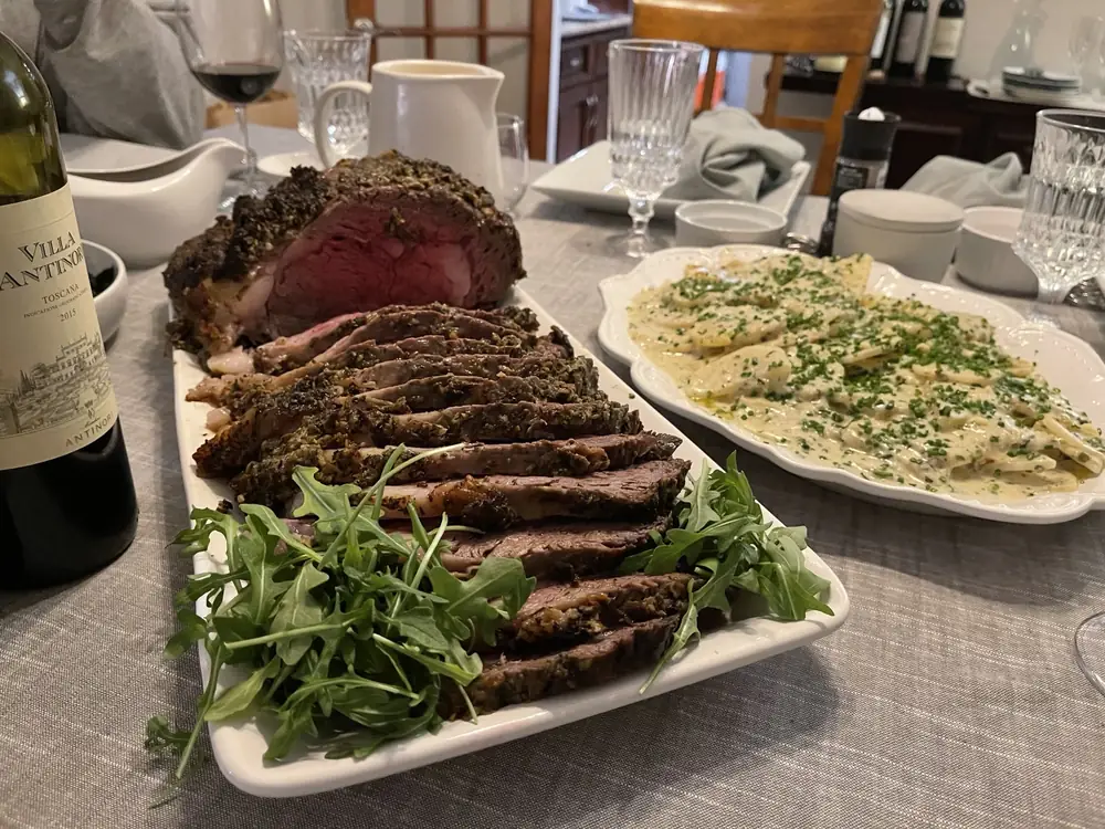 Family-style prime rib dinner platter with a composed side dish on a set dining table.