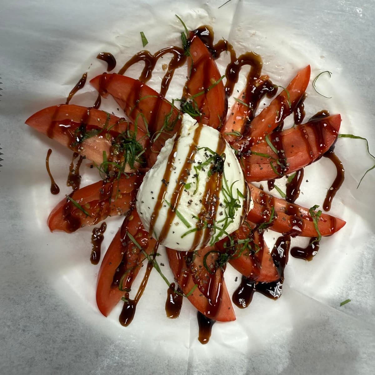 Burrata caprese plate finished with tomatoes, greens, and balsamic.